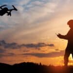 A silhouette of a soldier flying a drone at sunset.