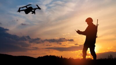 A silhouette of a soldier flying a drone at sunset.