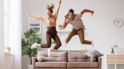 A happy young couple celebrate a win by jumping high above their new sofa.