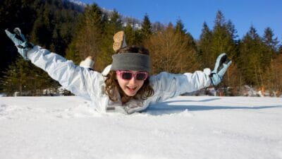 Girl sliding down on snow with arms spread out.