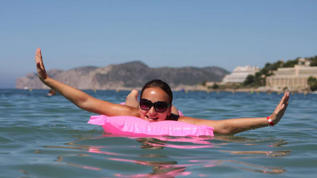 Happy woman relaxing on a pink floating mattress in sea.