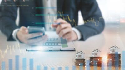 Shares vs property concept illustrated by graphs in the background and house models on coins.