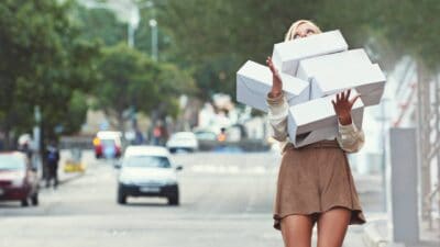 A woman carries a stack of boxes along a street after a big day of shopping