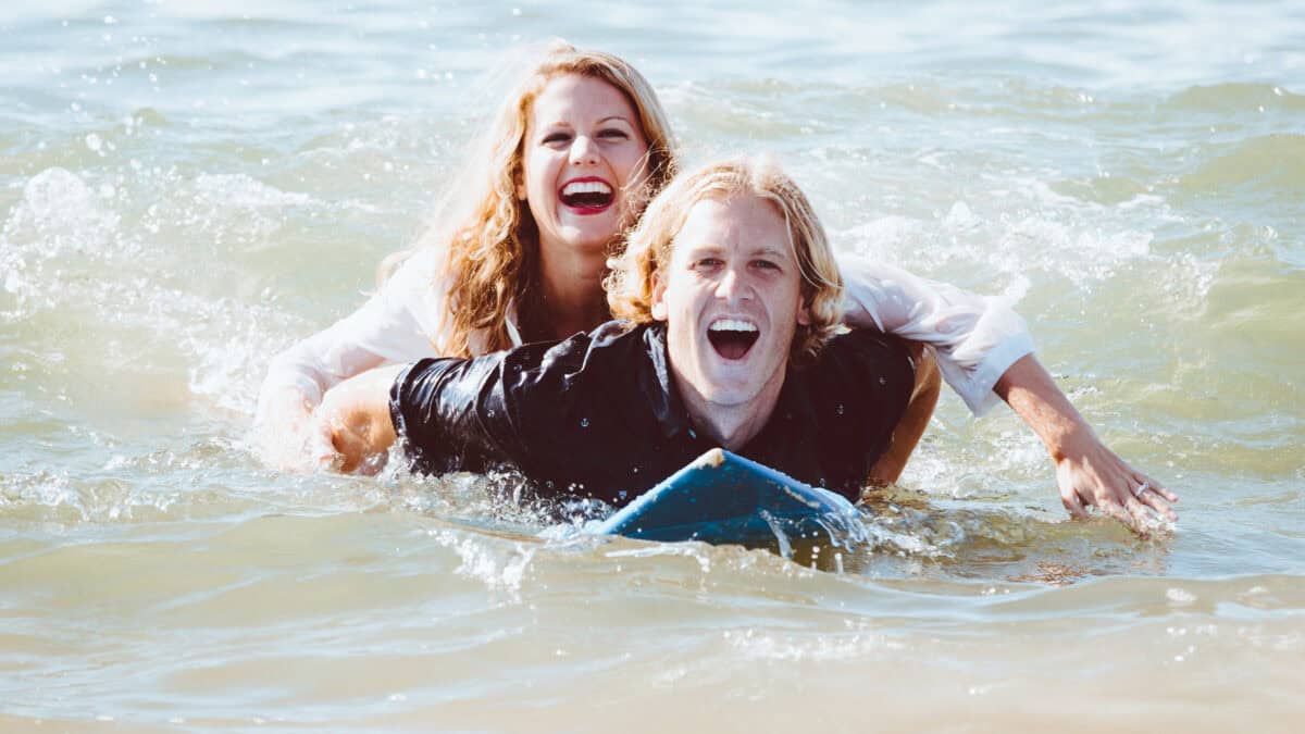 A happy laughing surfer couple surfing together.