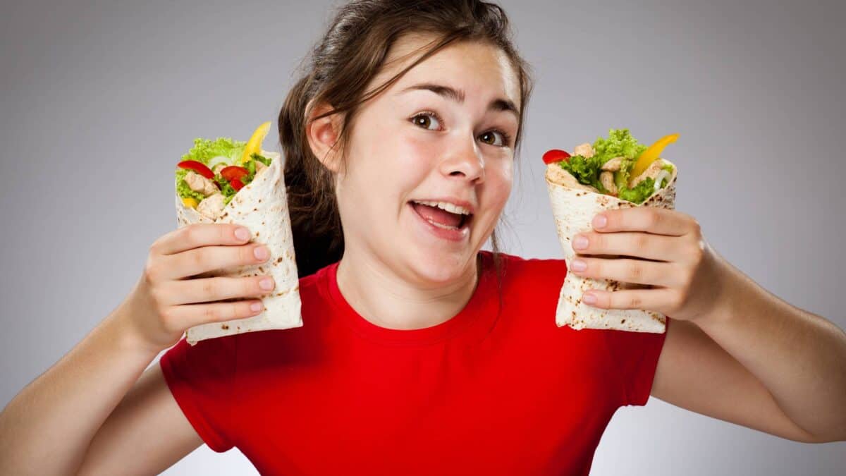 A happy young woman in a red t-shirt hold up two delicious burritos.