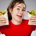 A happy young woman in a red t-shirt hold up two delicious burritos.