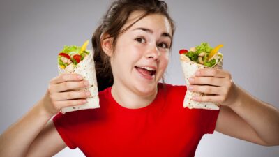 A happy young woman in a red t-shirt hold up two delicious burritos.