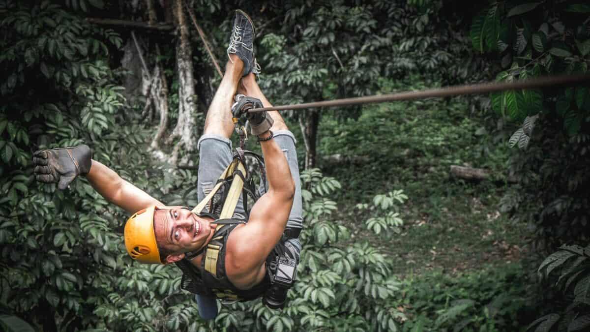 A cool dude looks back at the camera while ziplining above the treetops.