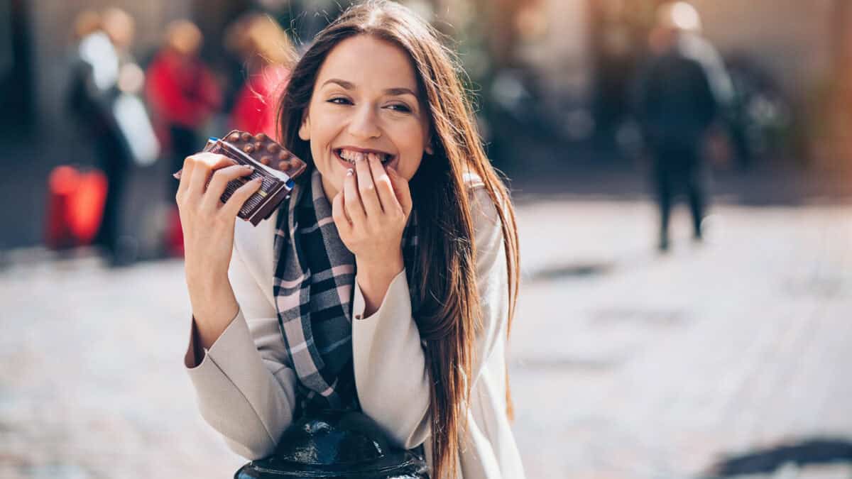 Smiling young woman eating chocolate outdoors.