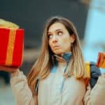 A bemused woman holds two presents of different sizes and colours and tries to make a choice.