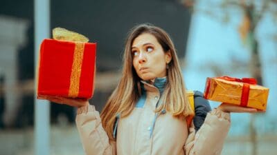 A bemused woman holds two presents of different sizes and colours and tries to make a choice.