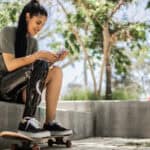 Disabled skateboarder woman using mobile phone at the park.