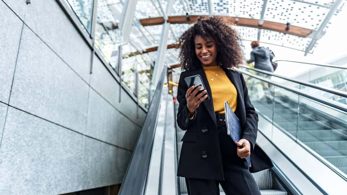 A woman wearing a yellow shirt smiles as she checks her phone.