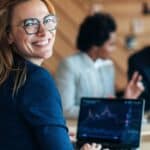 A woman presenting company news to investors looks back at the camera and smiles.