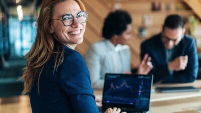 A woman presenting company news to investors looks back at the camera and smiles.