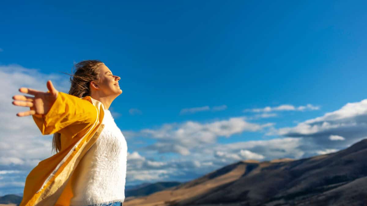 Happy woman stands with raised hands on background of sunset in mountain's range