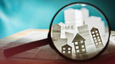 Magnifying glass in front of an open newspaper with paper houses.