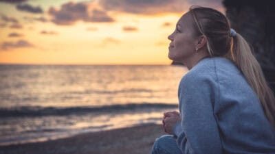 Smiling young woman looking with hope into horizon during sunset at beach.