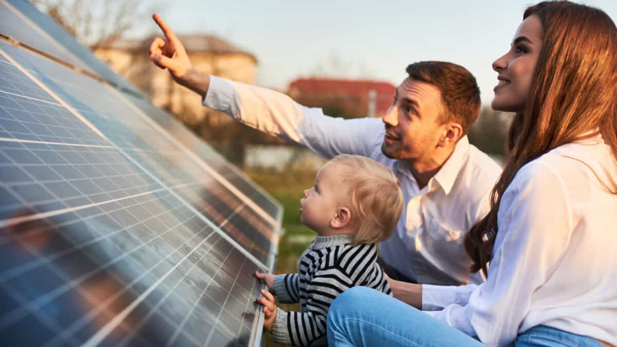 Young woman with a kid and a man in the sun rays look at the solar panels.