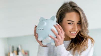 Happy young woman saving money in a piggy bank.