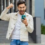 A young man punches the air in delight as he reacts to great news on his mobile phone.