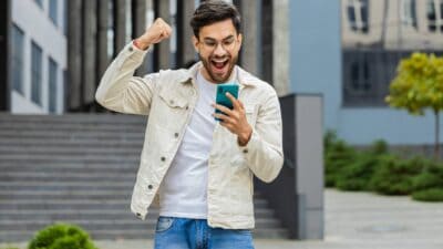 A young man punches the air in delight as he reacts to great news on his mobile phone.