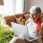 A happy elderly woman smiles and cheers as she looks at good investment news on her laptop.