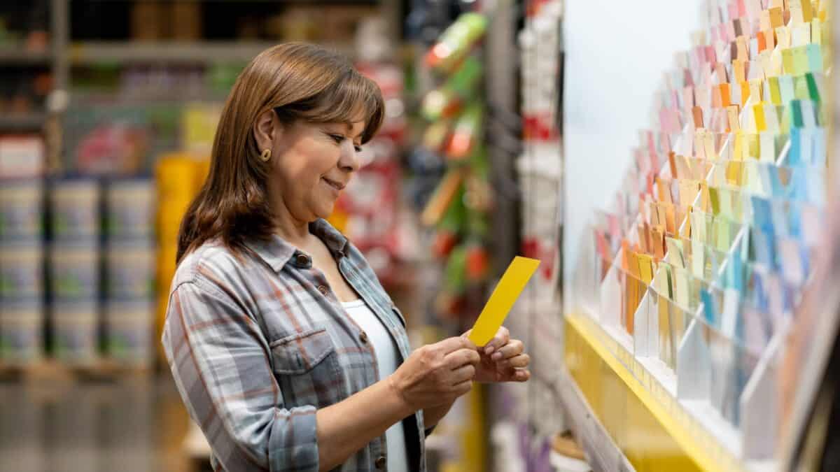 A smiling woman at a hardware shop selects paint colours from a wall display.