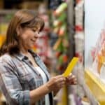 A smiling woman at a hardware shop selects paint colours from a wall display.