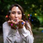 A woman blows what looks like colourful dust at the camera, indicating a positive or magic situation.