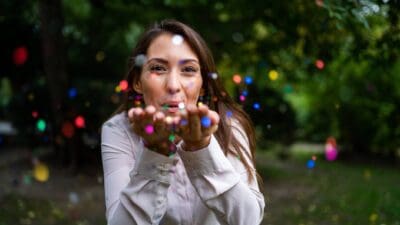 A woman blows what looks like colourful dust at the camera, indicating a positive or magic situation.