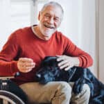 A disabled senior man in wheelchair playing with a pet dog at home.