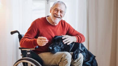 A disabled senior man in wheelchair playing with a pet dog at home.