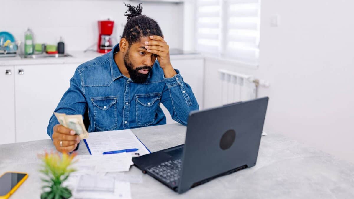 A man holds his head as he looks at his laptop and contemplates more bills to pay.