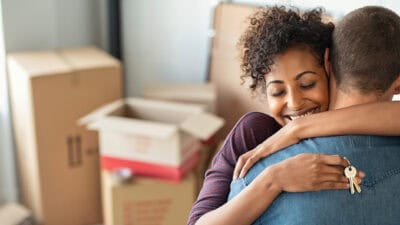 Happy couple hugging in their new house around cardboard boxes.