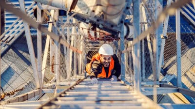 Oil industry worker climbing up metal construction and smiling.