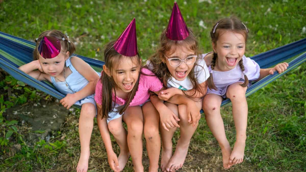 Four girls in festive pink hats are sitting on a hammock and laughing merrily.