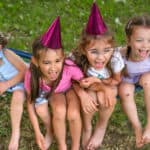 Four girls in festive pink hats are sitting on a hammock and laughing merrily.