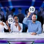 A panel of four judges hold up cards all showing the perfect score of ten out of ten