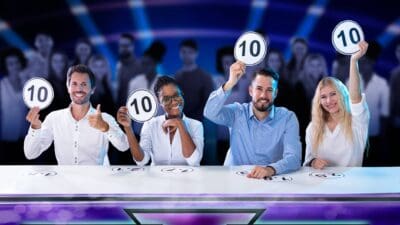 A panel of four judges hold up cards all showing the perfect score of ten out of ten