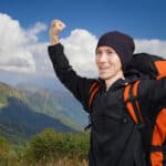 Hiker man backpacker with hands up in the summer mountains with cloudy sky.