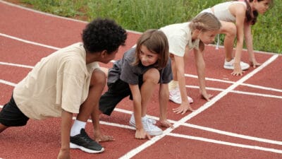 Two boys looking at each other while standing by start line on stadium against two schoolgirls.