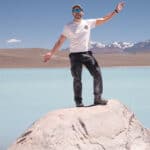 Man standing on rock next to turquoise salt lagoon.