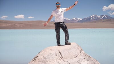 Man standing on rock next to turquoise salt lagoon.