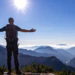 Man with backpack spreading his arms out and soaking in the sun.