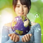 Woman with hands under a holographic globe with green related icons in the background.