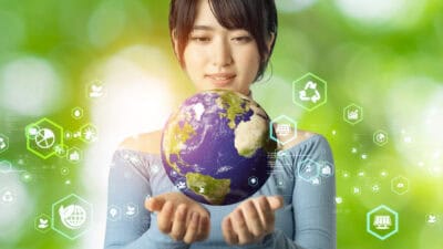 Woman with hands under a holographic globe with green related icons in the background.