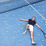 A man lays on a tennis court exhausted.