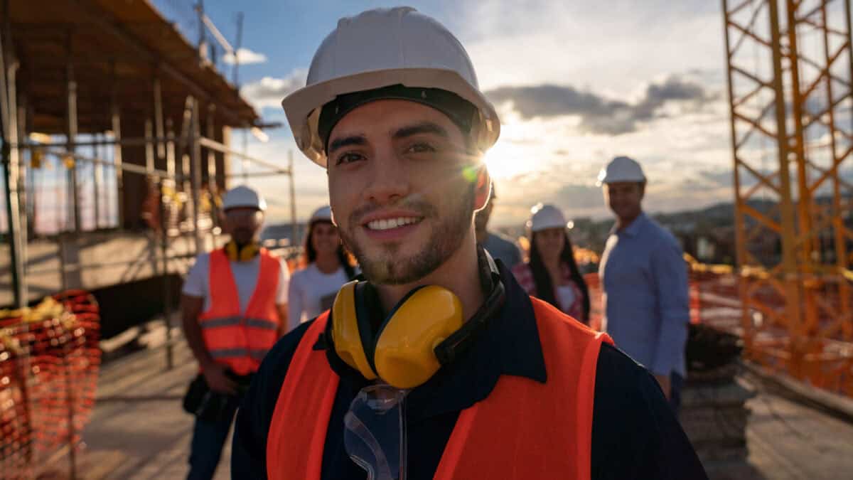 Happy construction worker at a building site with a group of workers at the background.