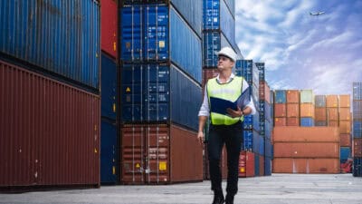 A transport worker walks alongside a stack of containers at a port.